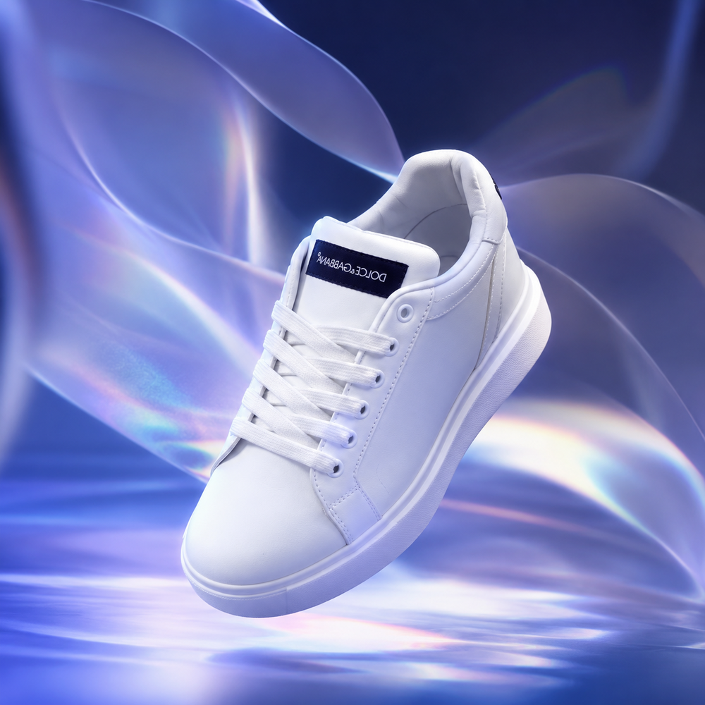 A white low-top sneaker with white laces and a black tongue label reading DOLCE&GABBI, floating against a blue and purple abstract fluid background.
